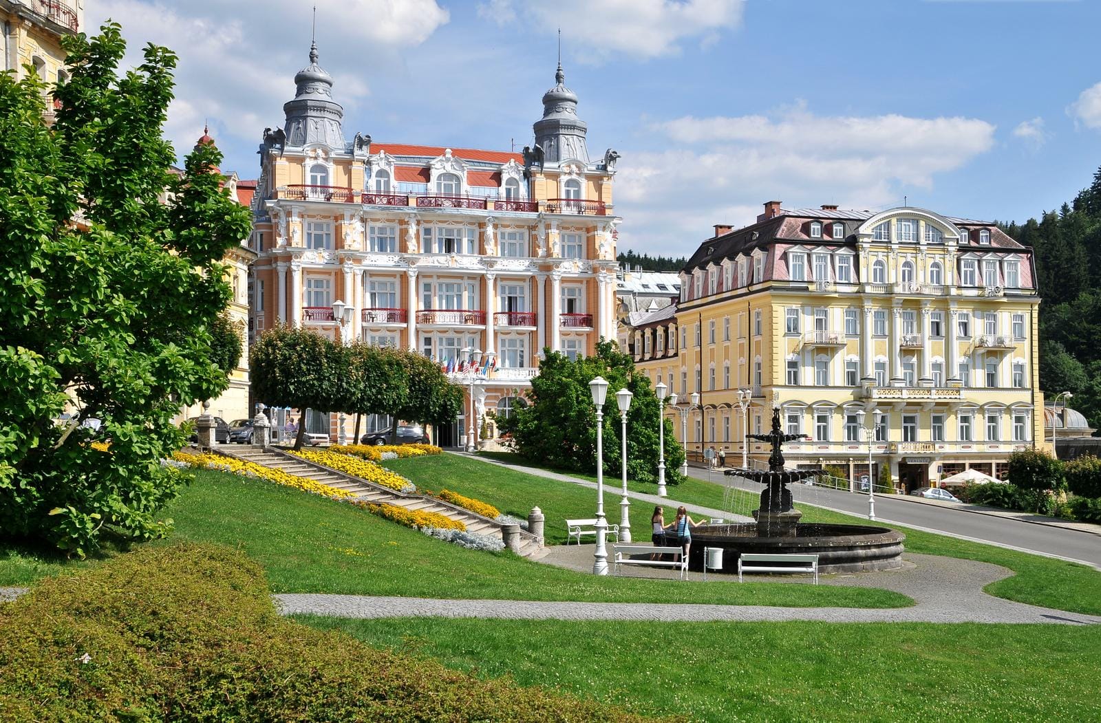 Historische Gebäude mit Türmen und gelber Fassade in einem grünen Park in Marienbad.