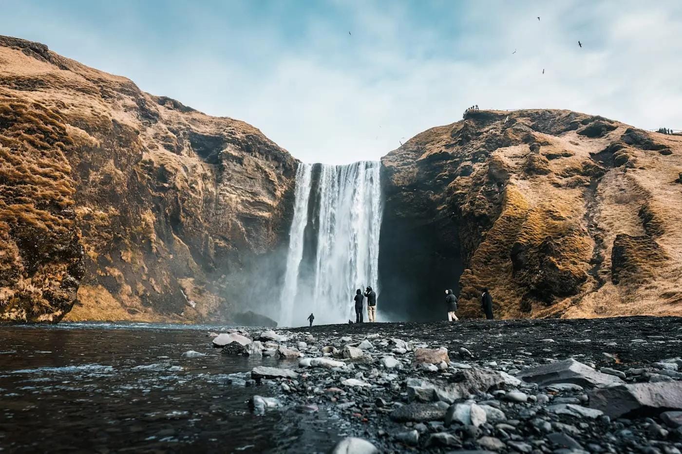 Wasserfall Skógafoss in Island, umgeben von moosbedeckten Felsen und klarem Himmel.