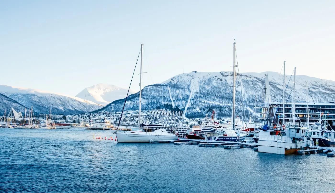 Winterhafen mit Segelbooten und verschneiten Bergen in Tromsø, Norwegen.