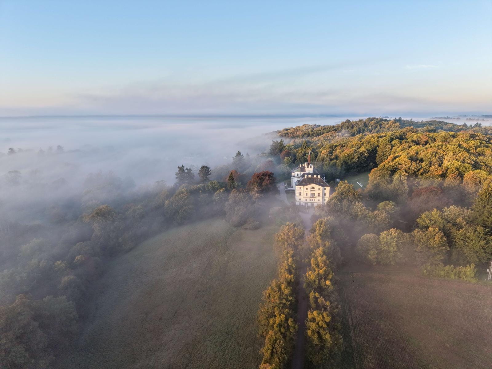 Schloss in nebeliger, herbstlicher Landschaft mit buntem Wald und Lichtungen.
