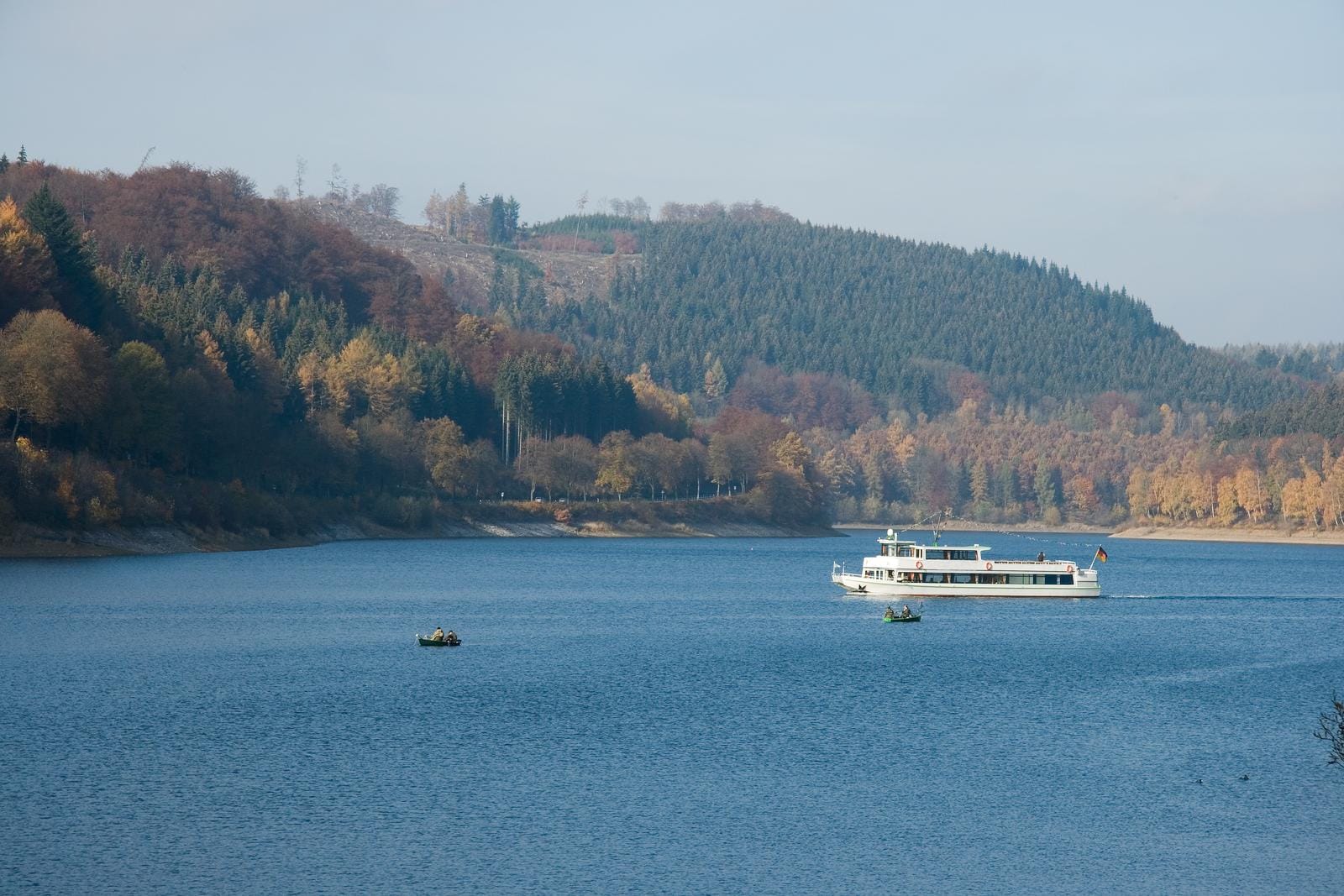 Herbstlicher See im Sauerland, Deutschland, mit Ausflugsboot und ruhigem Wasser.