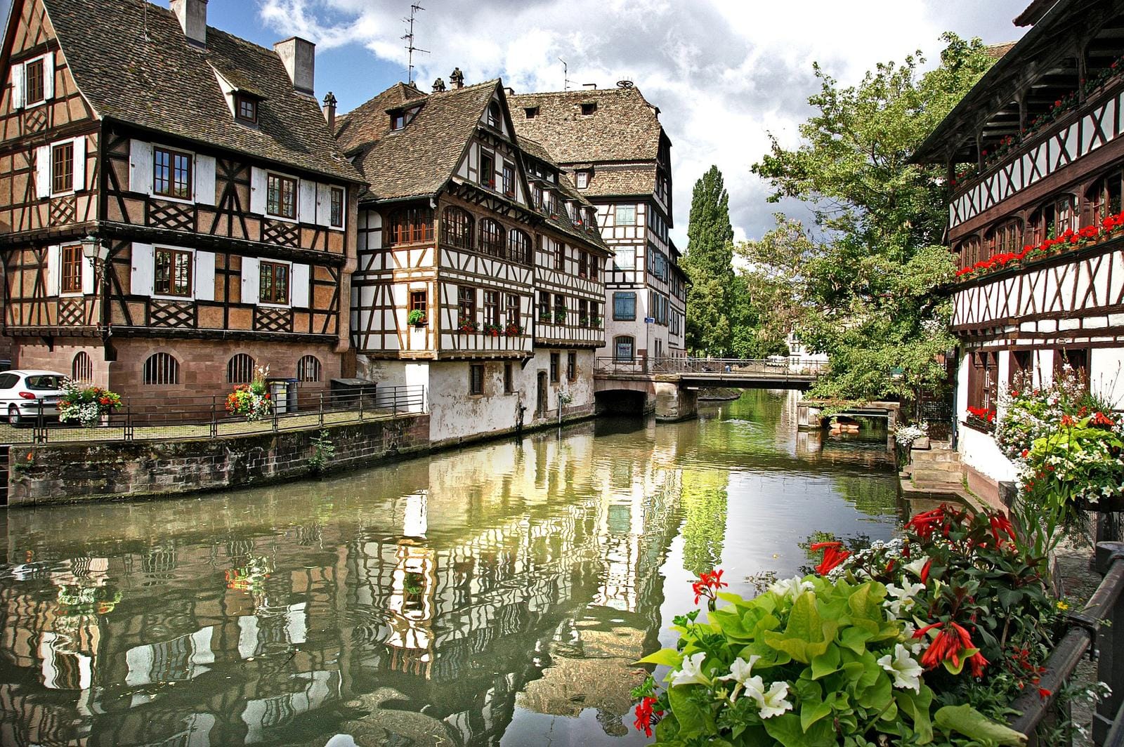 Fachwerkhäuser am Kanal in Straßburg, Frankreich mit blühenden Blumen und Brücke.