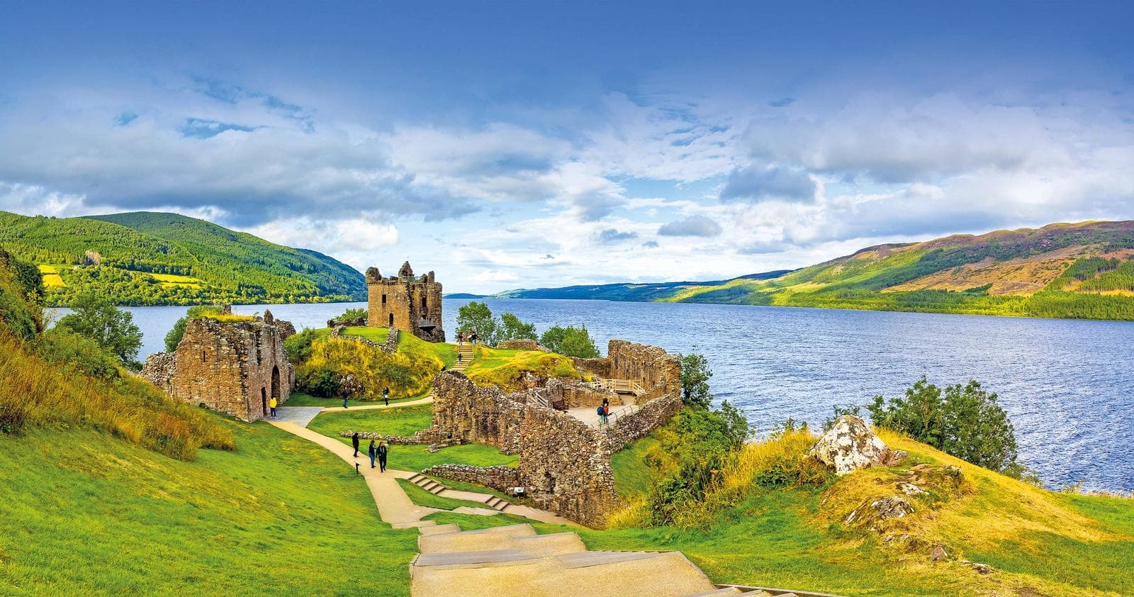 Schottland, Urquhart Castle am Loch Ness, umgeben von grünen Hügeln und blauem Himmel.